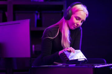 Female gamer in her 20s updating a gaming PC with headset on purple-lit studio setup