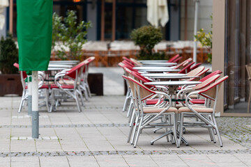 Outdoor cafe with empty red chairs and metal tables stands quietly on a paved street. Scene reflects calm atmosphere of low season and absence of visitors in urban setting