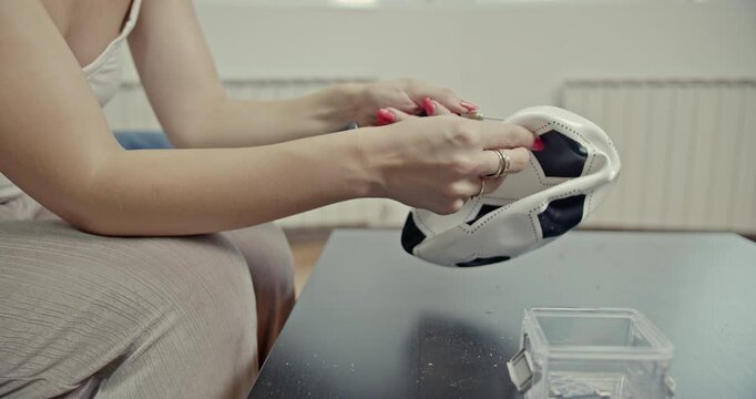 Close-up of a woman's hands using a pump to inflate a deflated football on a table at home. The video includes the audible sounds of the inflation process, emphasizing preparation and activity.