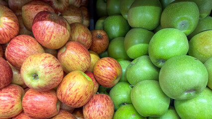 Close-up of bulk striped red and green apples (Malus domestica). Fresh fruits displayed for sale at a market or fair, separated by a dark divider.