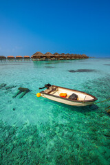 Fototapeta premium Tranquil closeup calm sea water waves with palm trees. Boat and bungalows background. Tropical island beach landscape exotic shore coast. Summer vacation, holiday amazing nature, Maldives.