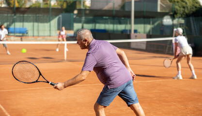 Elderly man and a woman with rackets in their hands play tennis together on a city court in the...