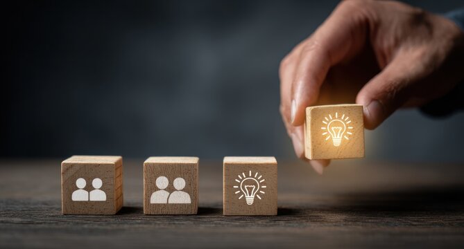 Hand places wooden cube with glowing idea symbol next to people icons.