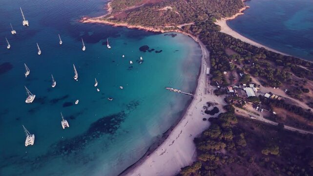 Segelschiffe liegen in einer Bucht der Mittelmeerinsel Korsika vor Anker. Ein malerischer Steg am langen Sandstrand komplettiert das Bild. Abendstimmung.