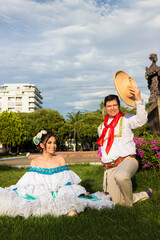 A Latina couple sits on green grass in traditional dress and looking at the camera, in downtown Neiva, Huila, Colombia. Concept of Colombian culture