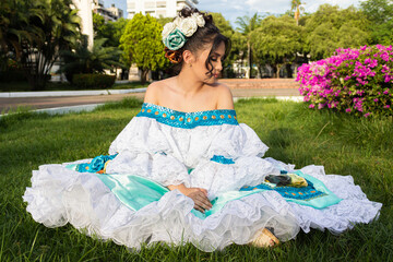 Portrait of a Hispanic female dancer in a traditional dress sitting on grass in Neiva, Huila, Colombia. Concept of Colombian culture