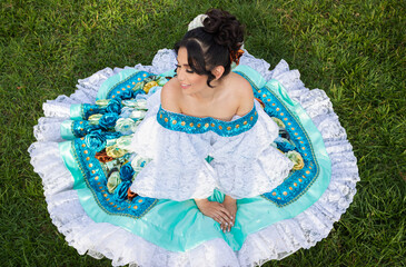 Portrait of a smiling Latina dancer in a traditional dress sitting on grass in Neiva, Huila, Colombia. Concept of Colombian culture
