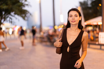 Fototapeta premium Elegant young woman walking on a lively promenade of Barceloneta at dusk