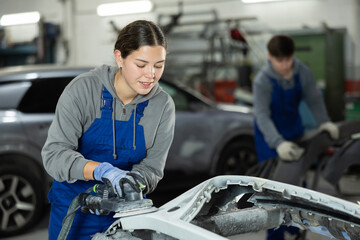 Woman auto mechanic using a grinding machine prepares car parts for painting