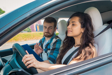 Smiling male instructor taking exam in young lady and showing thumbs up. Confident woman driving a car. Driving test, driver courses, exam concept