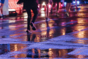 Fototapeta premium Night marathon runners crowd in the rain, sportsmen participants start running the half-marathon in the city streets with night lighting and illumination, group crowd of sportswomen joggers in motion