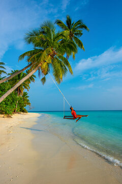 Tranquil closeup calm sea water waves with palm trees. Woman Swinging on the tree. Tropical island beach landscape exotic shore coast. Summer vacation, holiday amazing nature, Maldives.