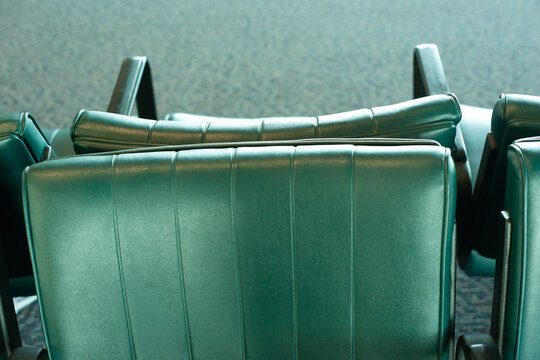 Back to back in close quarters while in public. Two green leather industrial bench style seats in an airport or bus terminal public transportation hub