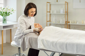 Portrait of happy beautiful woman lying on couch in cosmetology cabinet and receiving apparatus...