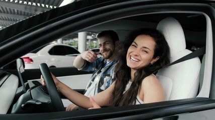 Happy woman and male instructor sitting in car, showing thumbs up. Slow motion