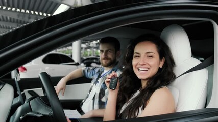 Happy woman holding key, sitting on the car with male instructor. Slow motion
