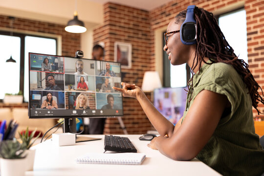 Black female manager uses headphones and computer in communicating with colleagues during virtual meeting. Self employed woman virtually presenting startup project with potential clients on video call