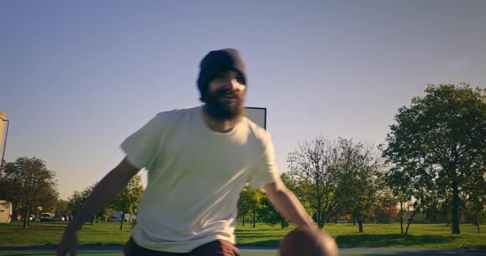 Slow motion of young man playing practice basketball on outdoor court at sunset at 1000 fps. Natural light, urban sport lifestyle and freedom concept. - Powered by Adobe