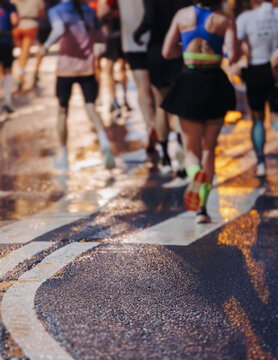 Night marathon runners crowd in the rain, sportsmen participants start running the half-marathon in the city streets with night lighting and illumination, group crowd of sportswomen joggers in motion