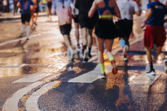 Night marathon runners crowd in the rain, sportsmen participants start running the half-marathon in the city streets with night lighting and illumination, group crowd of sportswomen joggers in motion