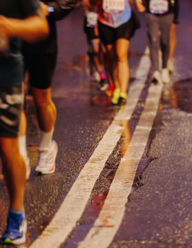 Night marathon runners crowd in the rain, sportsmen participants start running the half-marathon in the city streets with night lighting and illumination, group crowd of sportswomen joggers in motion