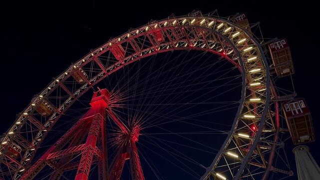 The Wiener Riesenrad, Illuminated giant Ferris Wheel glowing at night against dark sky at Prater Amusement Park, Vienna