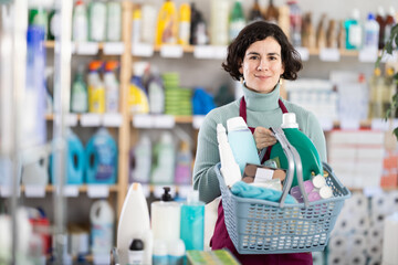 Positive middle-aged woman with full basket choosing something at household goods shop