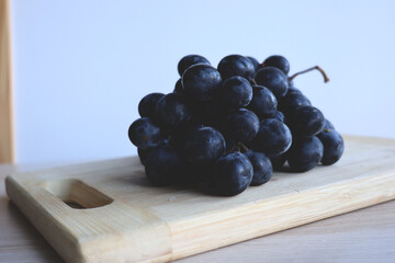 A close-up of a bunch of blue grapes lying on a rustic wooden board - Soft focus