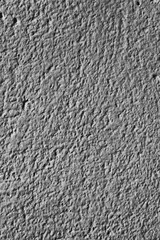 Rough gray cement wall texture with side lighting, showing details and shadows of the surface imperfections.