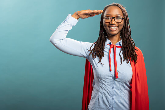 African american heroine standing confidently with a smile, showing respect and patriotism with her hand on her forehead. Cheerful black woman with glasses, looking and saluting at the camera.