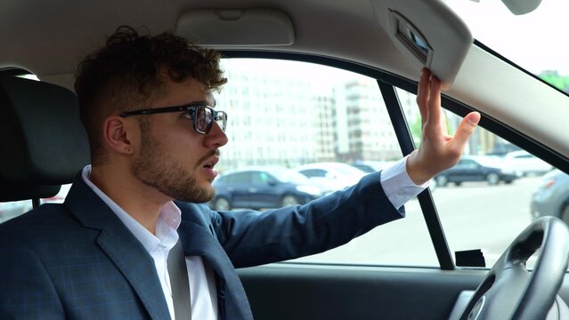 Young man sitting in his car on driver seat and looking at the mirror before the start of the trip. Transport, business and people concept. Slow motion - Powered by Adobe