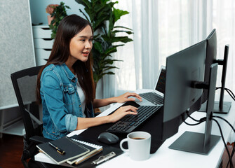 Smiling young Asian IT developer working software development information on pc screens and laptop, creating program coding for latest version application on website with firmware updated. Stratagem.