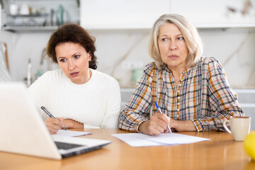 Obraz premium Attentive old and middle-aged women joining distant education using laptop in the kitchen