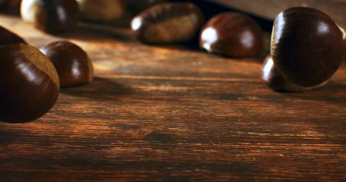 Slow motion close up of autumn chestnuts falling on rustic fabric and wood. Cozy, seasonal and organic atmosphere at 1000 fps.