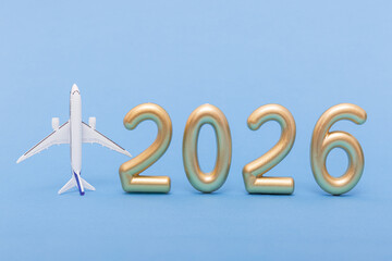 Airplane model and golden 2026 numbers on purple background. Symbol of travel plans and future holiday inspiration.