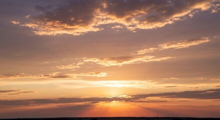 Sunset with golden, orange, and purple clouds above distant dark land