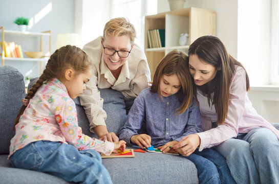 Three generation family, senior granny woman, mother, two kids sitting on sofa, playing with wooden shapes on board, interacting closely, smiling, enjoying shared activity and family connection fun