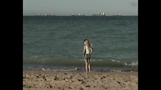 Young girl at edge of sea in vintage 90s vhs home video style
