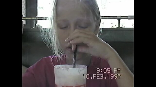 Young girl drinks pink milkshake in booth with soft retro vhs tone