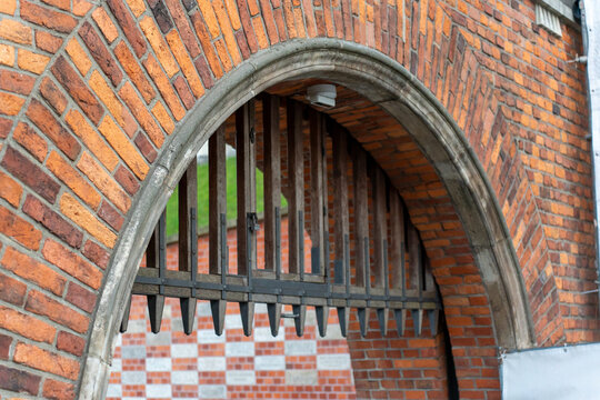 Historic brick archway with metal portcullis gate showing medieval fortress architecture and defensive construction with pointed iron spikes. Ancient security systems and castle fortification.