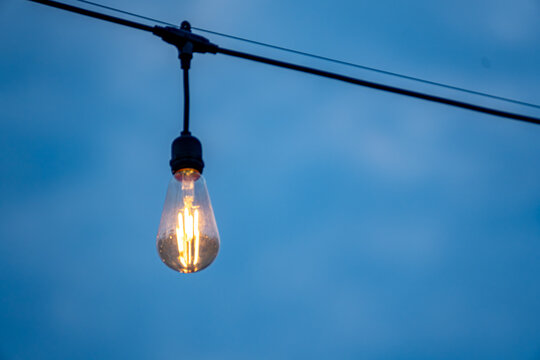 Edison-style light bulb on a string light fixture, hanging against a blue sky. This type of light bulb is known for its visible filament and vintage appearance. 