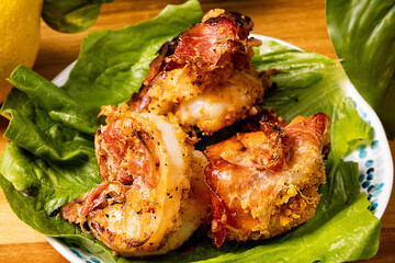 Grilled stuffed bacon wrapped black tiger shrimp on a lettuce leaf on a plate