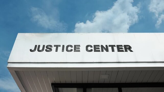 Justice Center word sign displayed on building facade under clear blue sky, representing legal administration, court services, and the centralized headquarters for the judicial system.