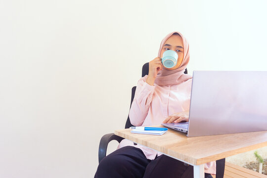 Young jilbab woman professional enjoying coffee while working