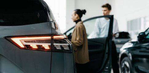 Modern car dealership interior featuring sleek vehicle design, illuminated taillights, and...