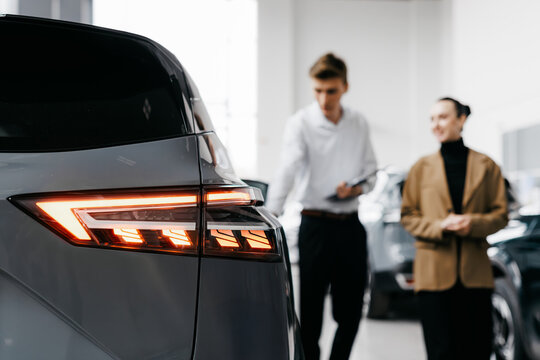 Car dealership scene featuring a smiling woman and a man discussing vehicle features, showcasing modern automotive design and customer engagement in a bright showroom environment - Powered by Adobe