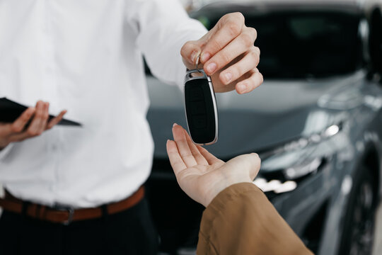 Salesperson handing over car keys to customer in a dealership, showcasing the excitement of new car ownership and the professional car sales experience