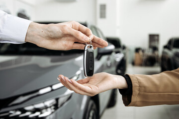 Hands exchanging car keys in a dealership, showcasing the excitement of a new car purchase, with modern vehicles in the background and a bright, inviting atmosphere