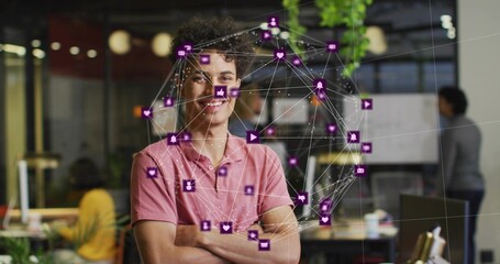 Standing man wearing pink polo and jeans crossing arms in startup office with network overlay icons