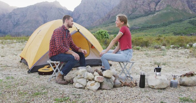 Sitting couple wearing flannel and red shirts camping at foothill, with yellow dome tent, fire pit - Powered by Adobe